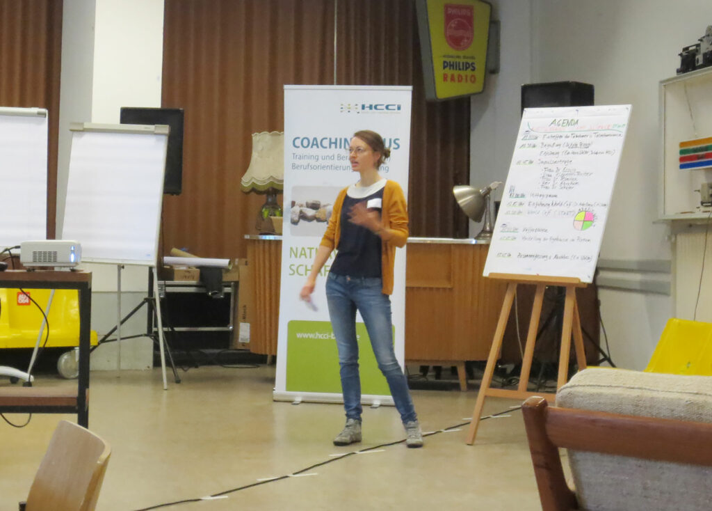 Frau in legerer Kleidung vor Flip-Chart stehend hält einen Vortrag; Eindrücke vom Networking-Camp Science 1.0 des HCCI, Institut für Supervision in Berlin